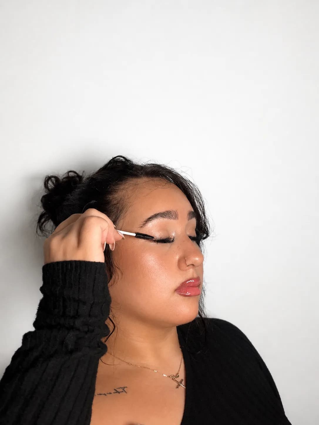 Anna brushing her lashes with a spoolie, eyes closed, against a bright white wall