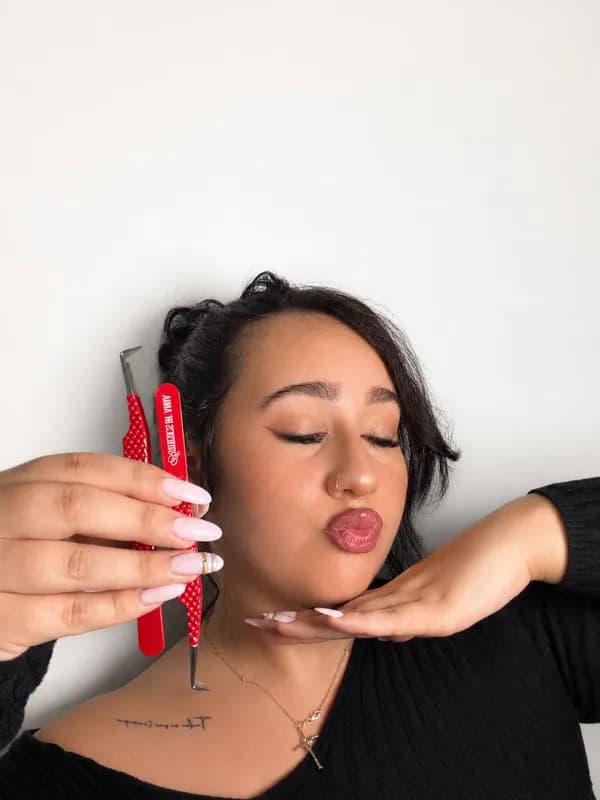 Anna blowing a kiss while holding her red Esthetics by Anna lash tweezers